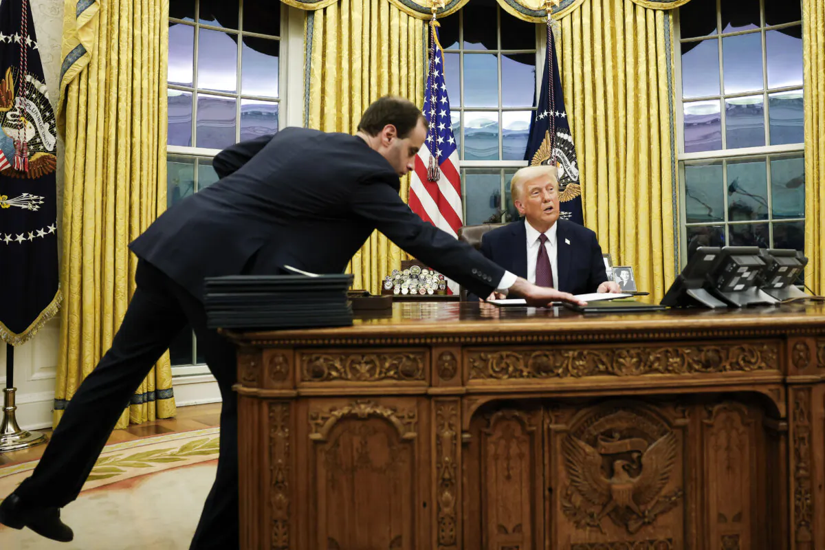 An aide hands U.S. President Donald Trump an executive order to sign in the Oval Office of the White House in Washington, DC, on Jan. 20, 2025. (Anna Moneymaker/Getty Images)