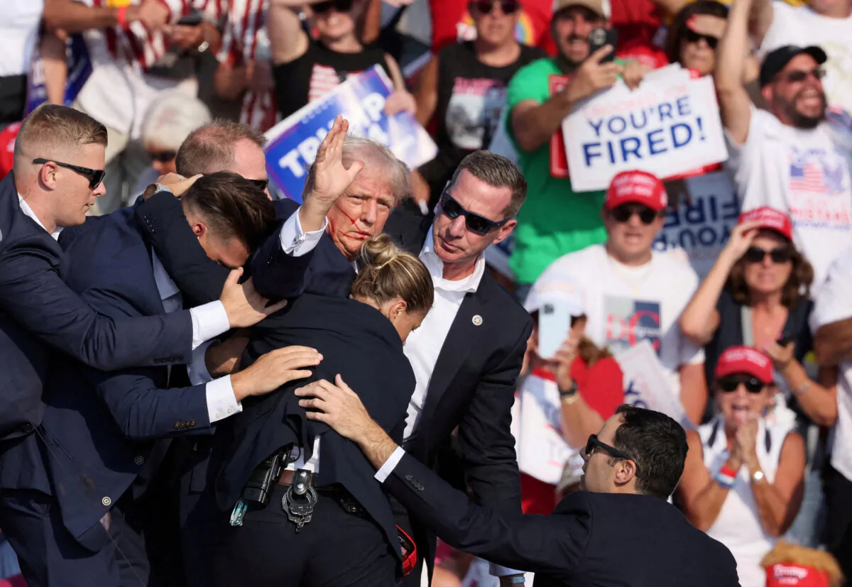 Then-presidential candidate Donald Trump gestures with a bloodied face while he is assisted by Secret Service personnel after he was shot in the right ear during a campaign rally at the Butler Farm Show in Butler, Pa., on July 13, 2024. (Brendan McDermid/Reuters)