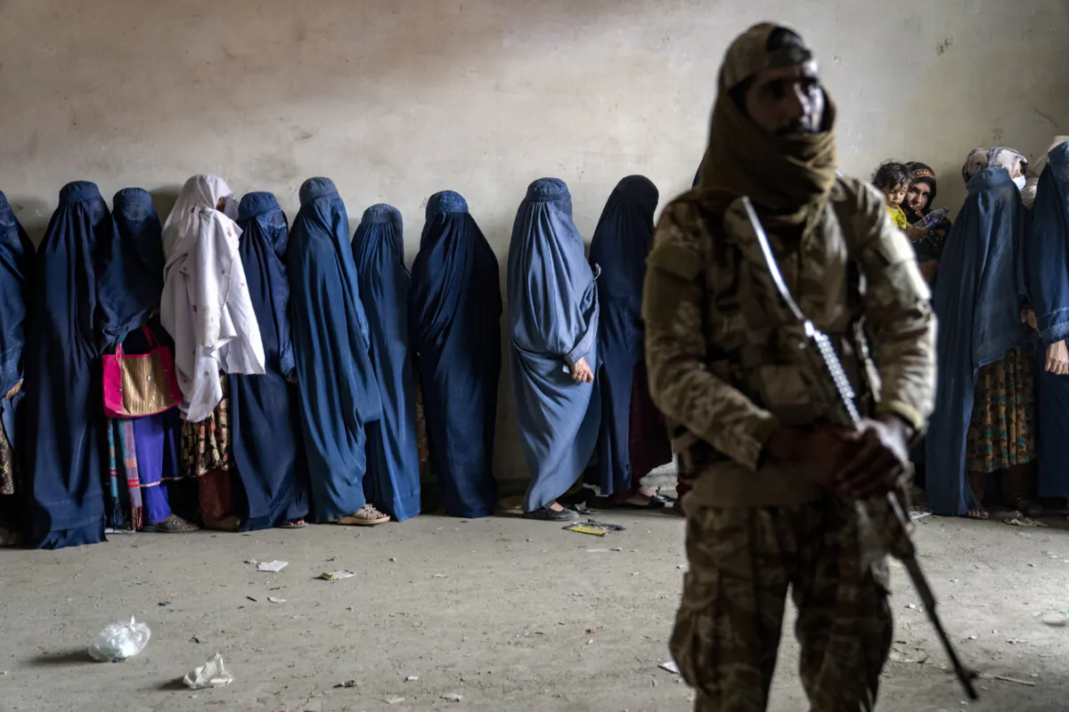 A Taliban fighter stands guard as women wait to receive food rations distributed by a humanitarian aid group in Kabul, Afghanistan, on May 23, 2023. (Ebrahim Noroozi/AP)