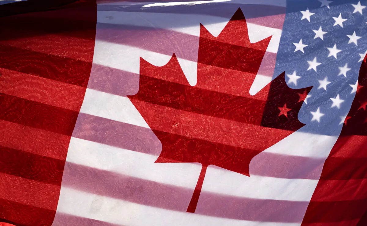 Sunlight shines through the flags of Canada and the United States, held together by a protester outside on Parliament Hill in Ottawa, on Feb. 1, 2025. (The Canadian Press/Justin Tang)