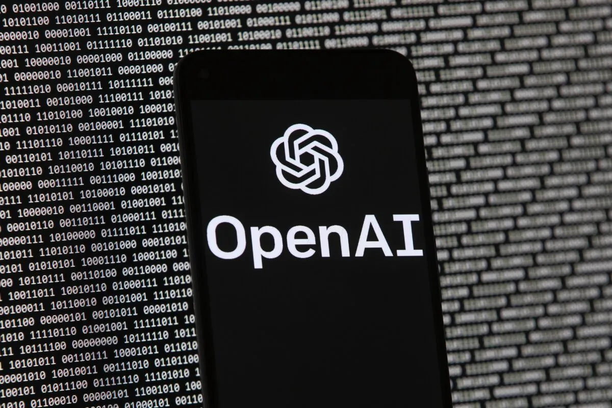 The OpenAI logo is seen on a mobile phone in front of a computer screen with random binary data, in Boston on March 9, 2023. (Michael Dwyer/AP Photo)
