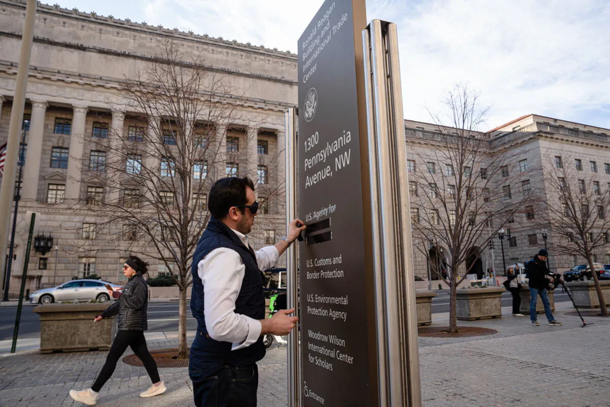 A person takes off the tape covering the U.S. Agency for International Development (USAID) in Washington on Feb. 7. 2025. (Madalina Vasiliu/The Epoch Times)