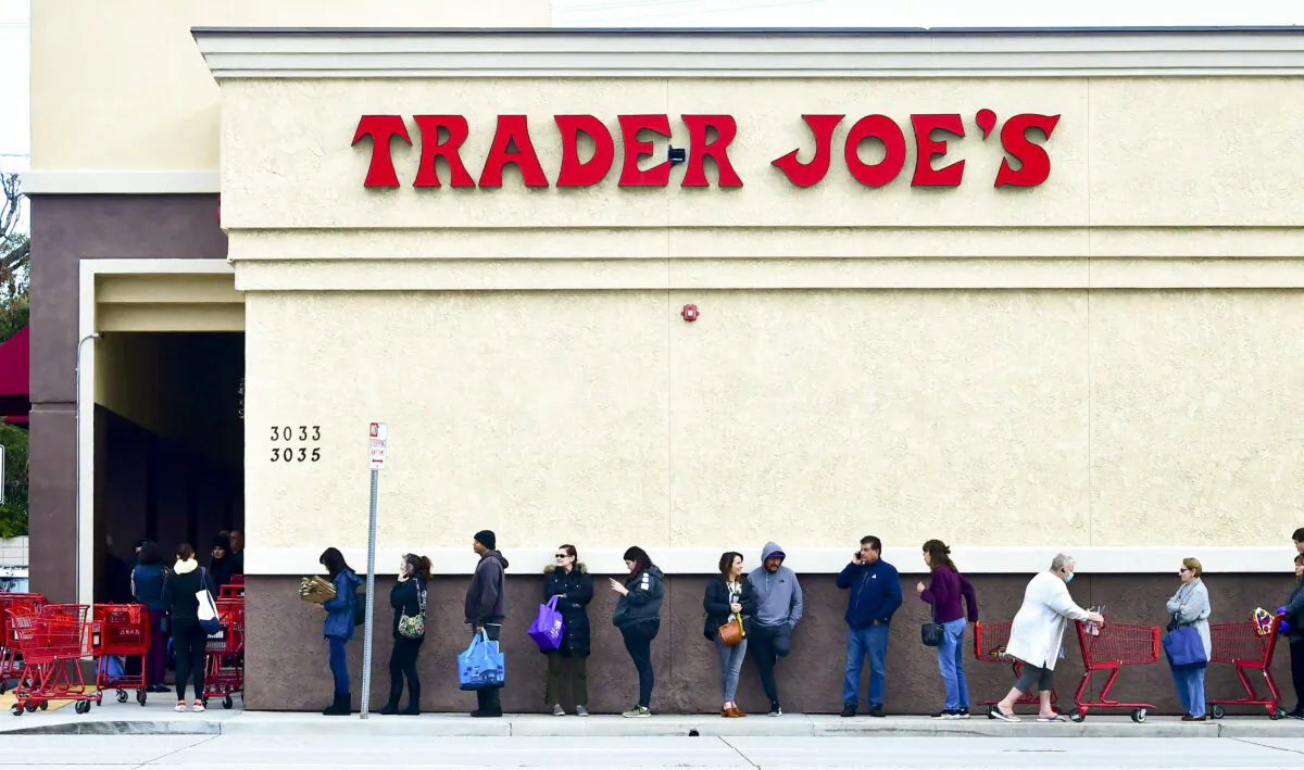 A woman wearing a facemask pushes her cart to the back of the line as people line up before the opening of a Trader Joe's store in Pasadena, Calif., on March 18, 2020.(Frederic Brown / AFP via Getty Images)