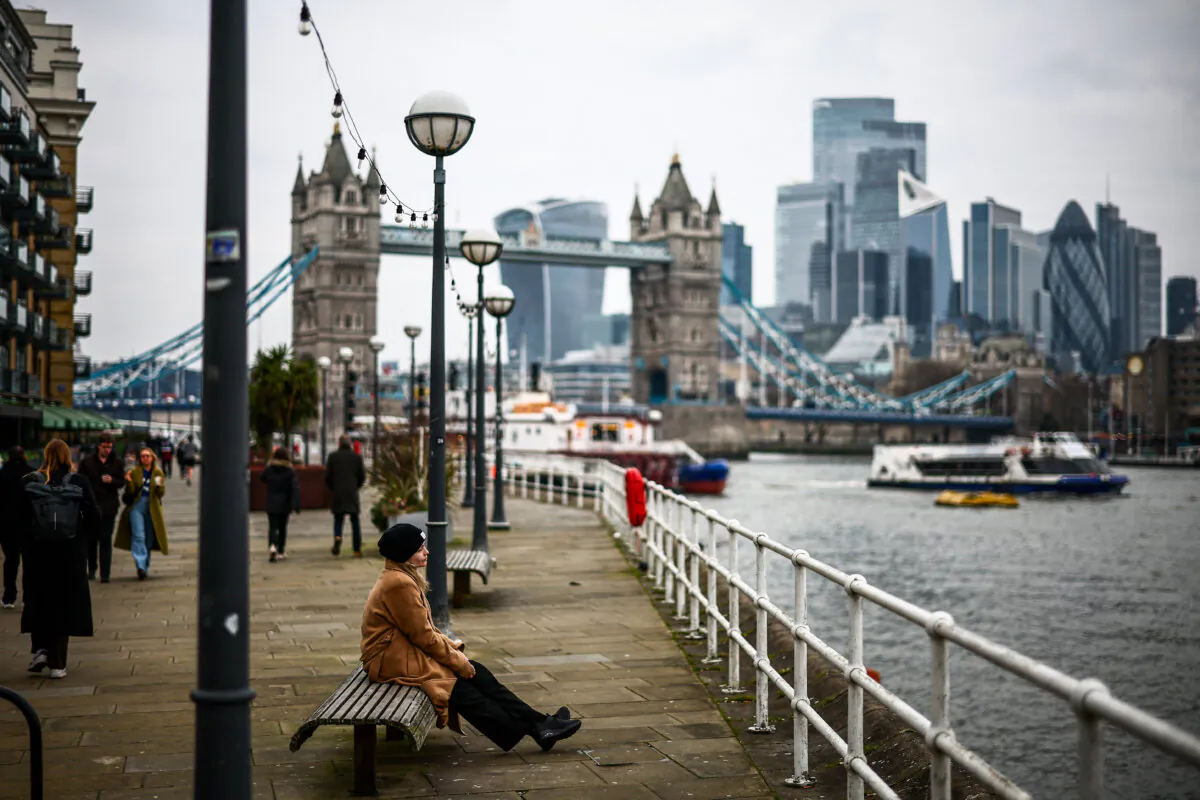 A person sits on a bench next to the River Thames backdropped by the City of London financial district and Tower Bridge in London on Feb. 13, 2025. (Henry Nicholls/AFP via Getty Images)