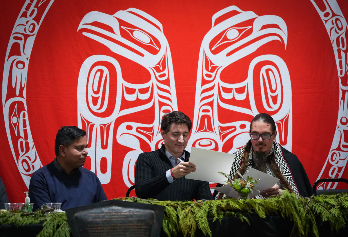 Prime Minister Justin Trudeau and Haida Nation President Gaagwiis Jason Alsop (R) sign documents as Minister of Crown-Indigenous Relations and Northern Affairs Gary Anandasangaree (L) watches during a community gathering to celebrate a land title agreement, in Skidegate on Haida Gwaii, B.C., on Feb. 17, 2025. The federal government will recognize Aboriginal title over the archipelago of Haida Gwaii off British Columbia’s northern coast in a historic agreement with the Haida First Nation. (The Canadian Press/Darryl Dyck)