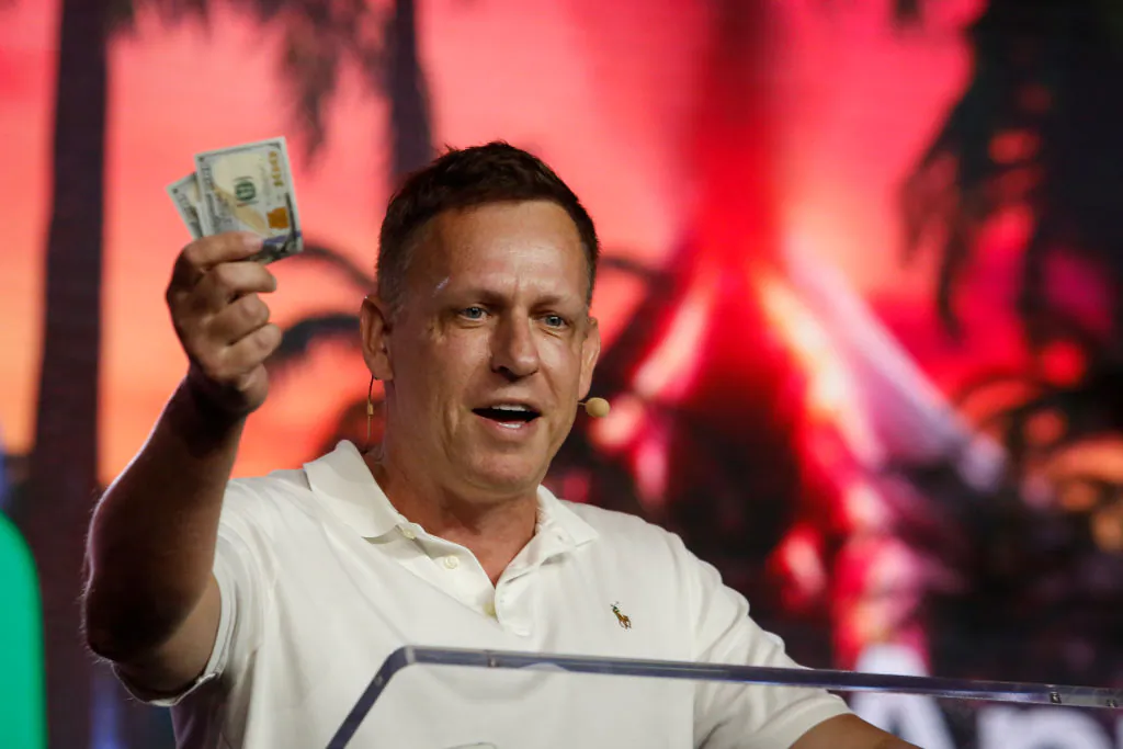 Peter Thiel, co-founder of PayPal, Palantir Technologies, and Founders Fund, holds hundred dollar bills as he speaks during the Bitcoin 2022 Conference at Miami Beach Convention Center in Miami, Fla., on April 7, 2022. (Marco Bello/Getty Images)