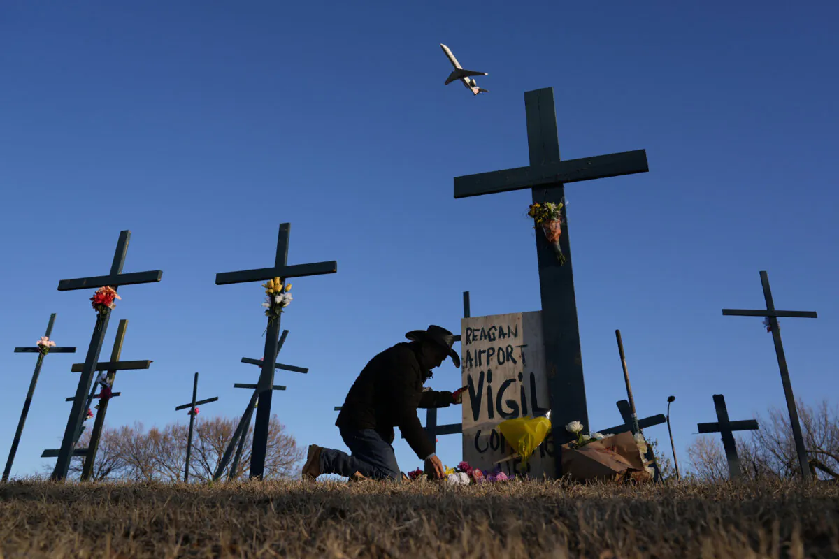 A plane takes off from Ronald Reagan Washington National Airport as Roberto Marquez of Dallas places flowers at a memorial of crosses he erected for the 67 victims of a midair collision between an Army helicopter and an American Airlines jet, on Feb. 1, 2025, in Arlington, Va. (AP Photo/Carolyn Kaster)