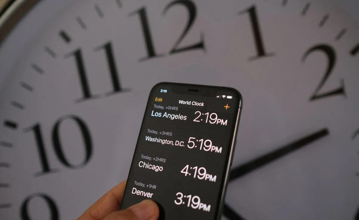 A clock behind a smartphone showing the time after daylight saving time was implemented in Los Angeles on March 15, 2022. (Chris Delmas/AFP via Getty Images)