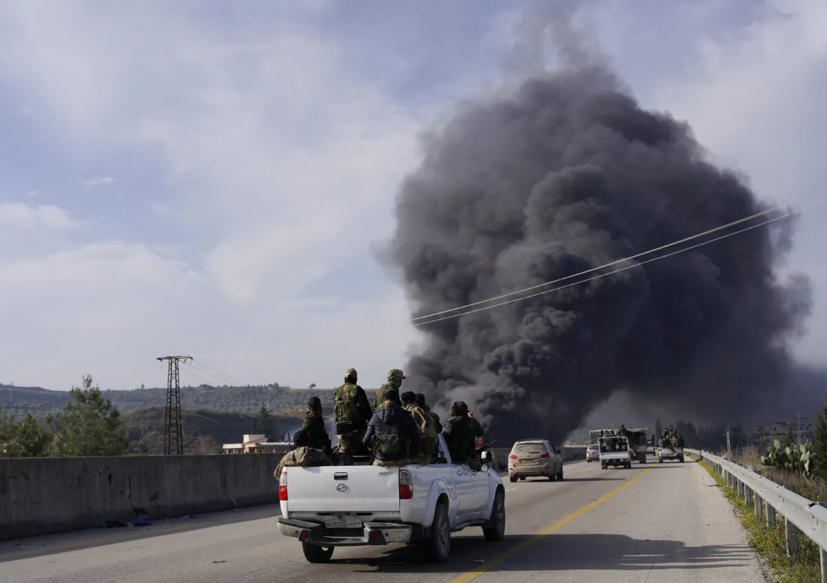 Smoke rises while members of the Syrian forces ride on a vehicle as they battle against a nascent insurgency by fighters from ousted leader Bashar al-Assad's Alawite sect, in Latakia, Syria March 7, 2025. REUTERS/Karam al-Masri