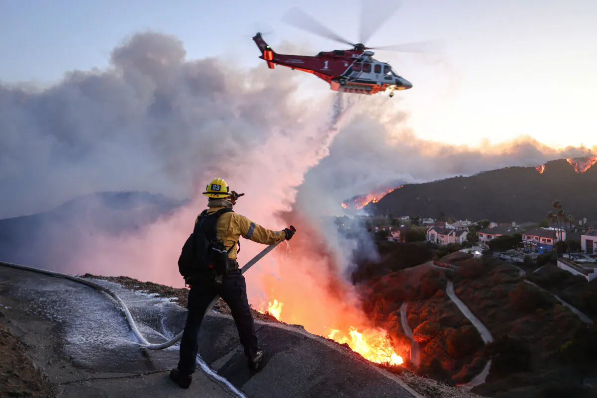 Fire personnel respond to homes destroyed while a helicopter drops water as the Palisades Fire grows in Pacific Palisades, Calif. on Jan. 7, 2025. (David Swanson/AFP via Getty Images)