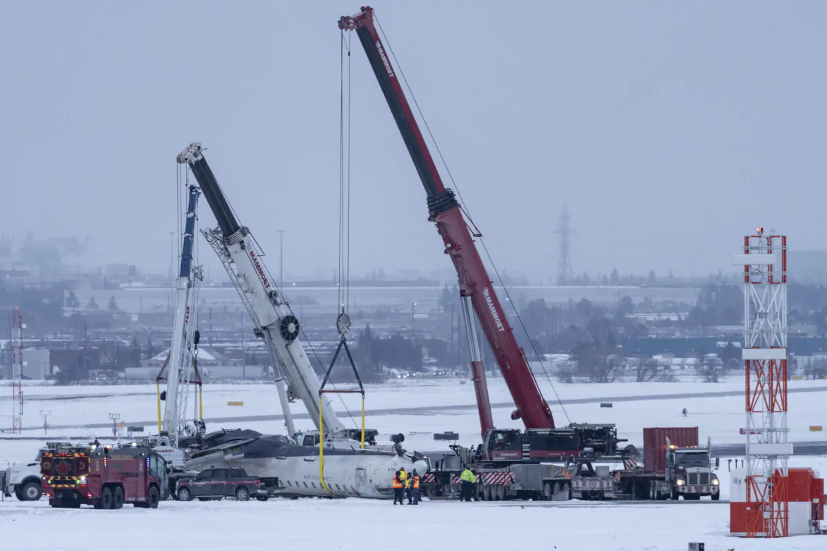 Cranes are positioned to remove the wreckage of Delta Flight 4819 from the runway at Toronto Pearson International Airport, in Mississauga, Ont., on Feb. 19, 2025. (The Canadian Press/Arlyn McAdorey)