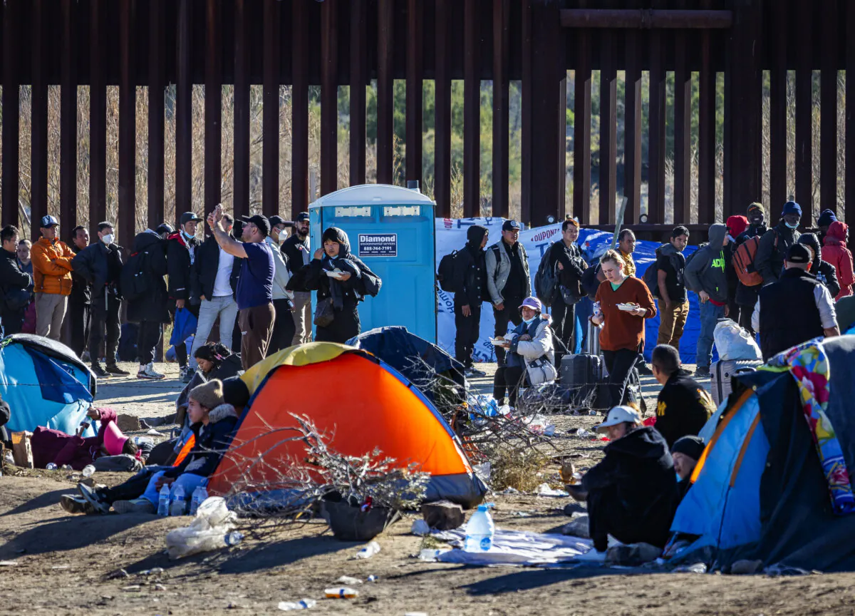Migrants who illegally crossed into the United States await processing by US Border Patrol agents outside of San Diego, Calif., on Dec. 5, 2023. (John Fredricks/The Epoch Times)