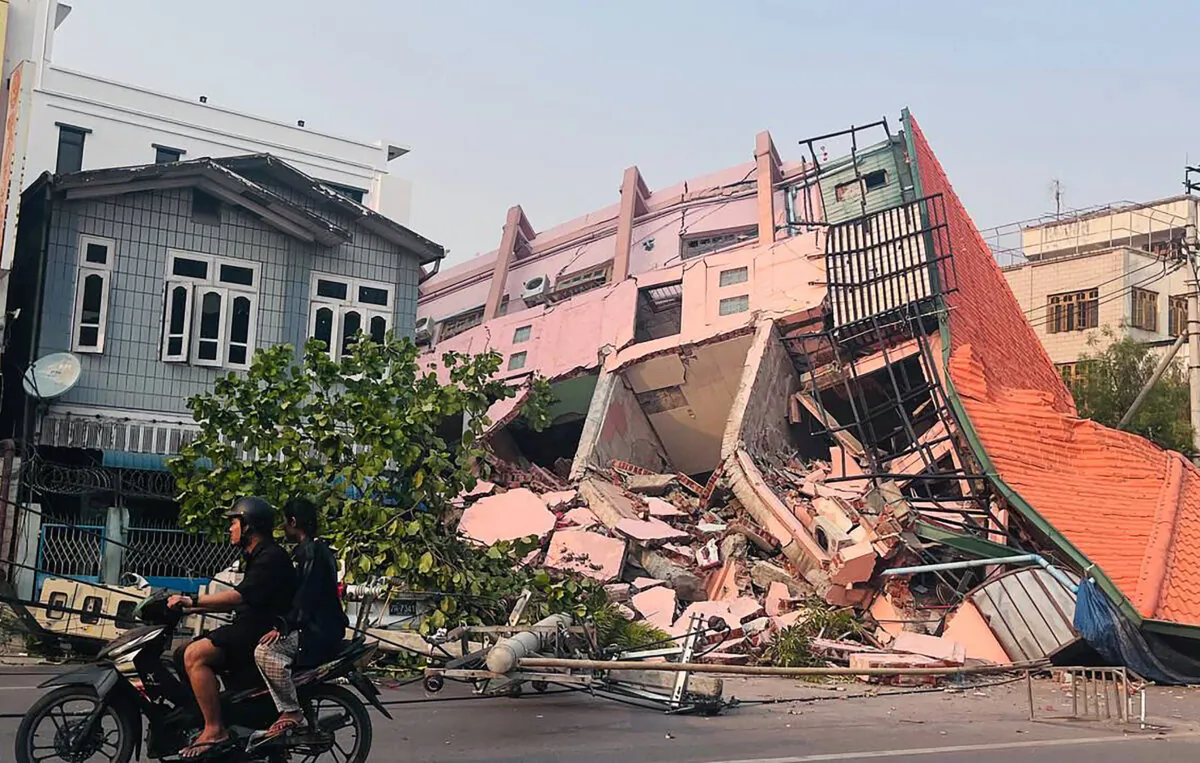 People drive on a motorbike past a collapsed building in Mandalay on March 28, 2025, after an earthquake in central Burma. (STR/AFP via Getty Images)