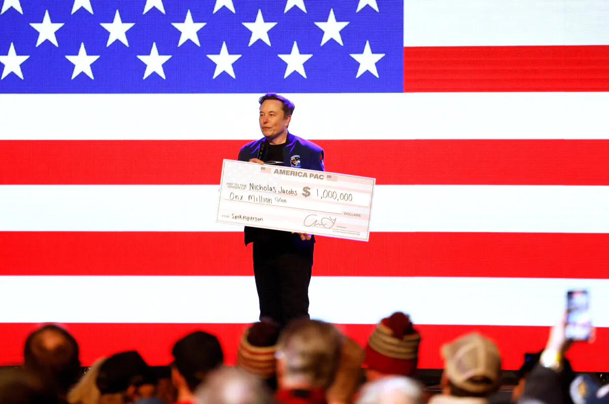 Elon Musk holds a check for $1 million dollars to Nicholas Jacobs, chairman of the Wisconsin College Republicans, at a town hall in Green Bay, Wis.,  on March 30, 2025. (Jeffrey Phelps/AP Photo)