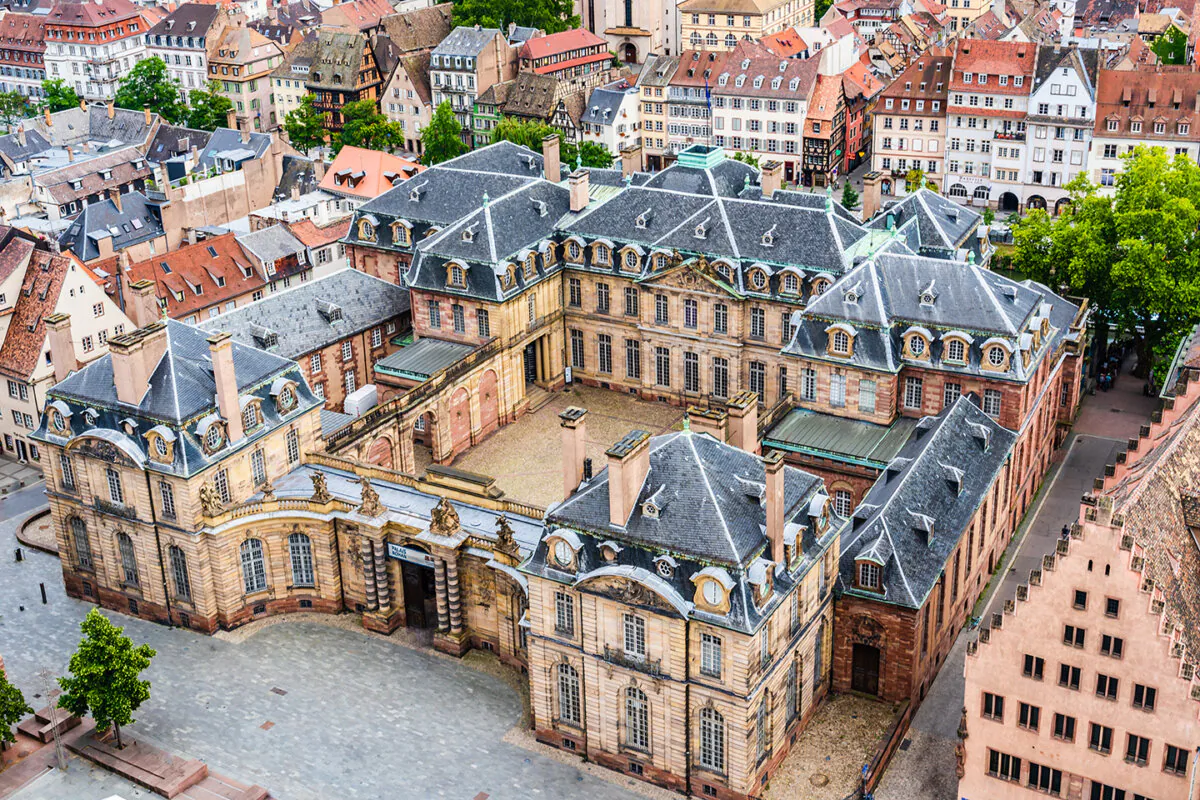 An aerial view of the Rohan Palace in Strasbourg shows the Parisian-style, hôtel particulier design with a walled courtyard. What appears to be the palace's main doorway is the courtyard entrance through a pavilion on the street. The palace is primarily built with yellow sandstone from Wasselonne, a town in Bas-Rhin, France, and pink sandstone is used for the less visible architectural elements. (PhotoFires/Shutterstock)