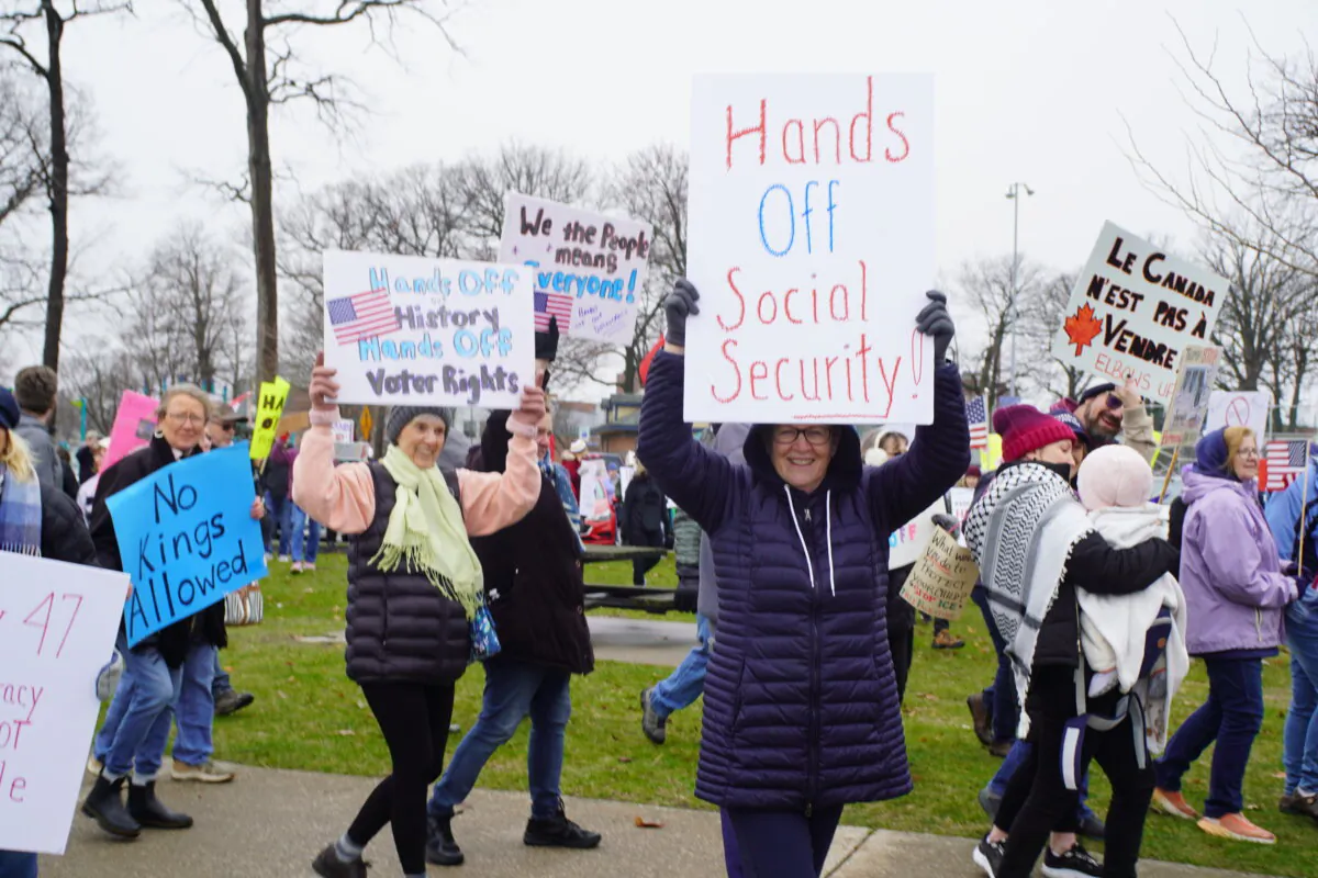 Protesters hold signs at a "Mobilization Day" rally in Port Huron, Mich. on April 5, 2025. (Steven Kovac/Epoch Times)
