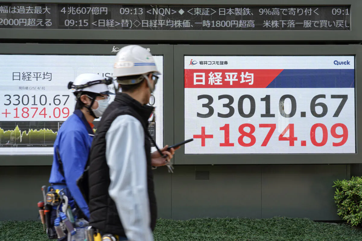Workers walk past an electronic board showing the numbers of the Nikkei Stock Average on the Tokyo Stock Exchange along a street in Tokyo on April 8, 2025. (Kazuhiro Nogi/AFP)