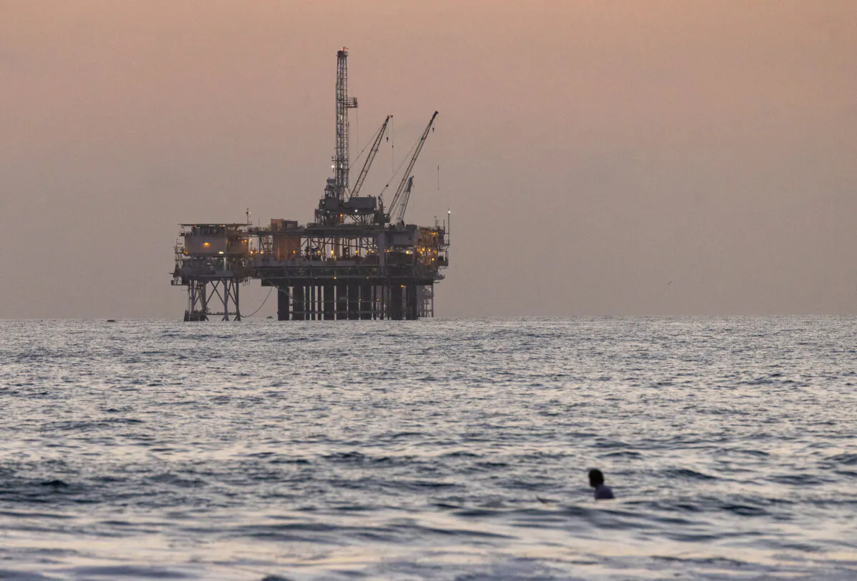 An oil rig sits in the background of surfers in Huntington Beach, Calif., on Sept. 12, 2024. (John Fredricks/The Epoch Times)