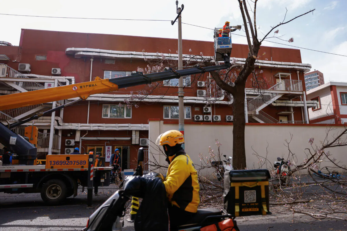 Emergency team members cut off tree branches following strong winds, in Beijing on April 12, 2025. (Tingshu Wang/Reuters)