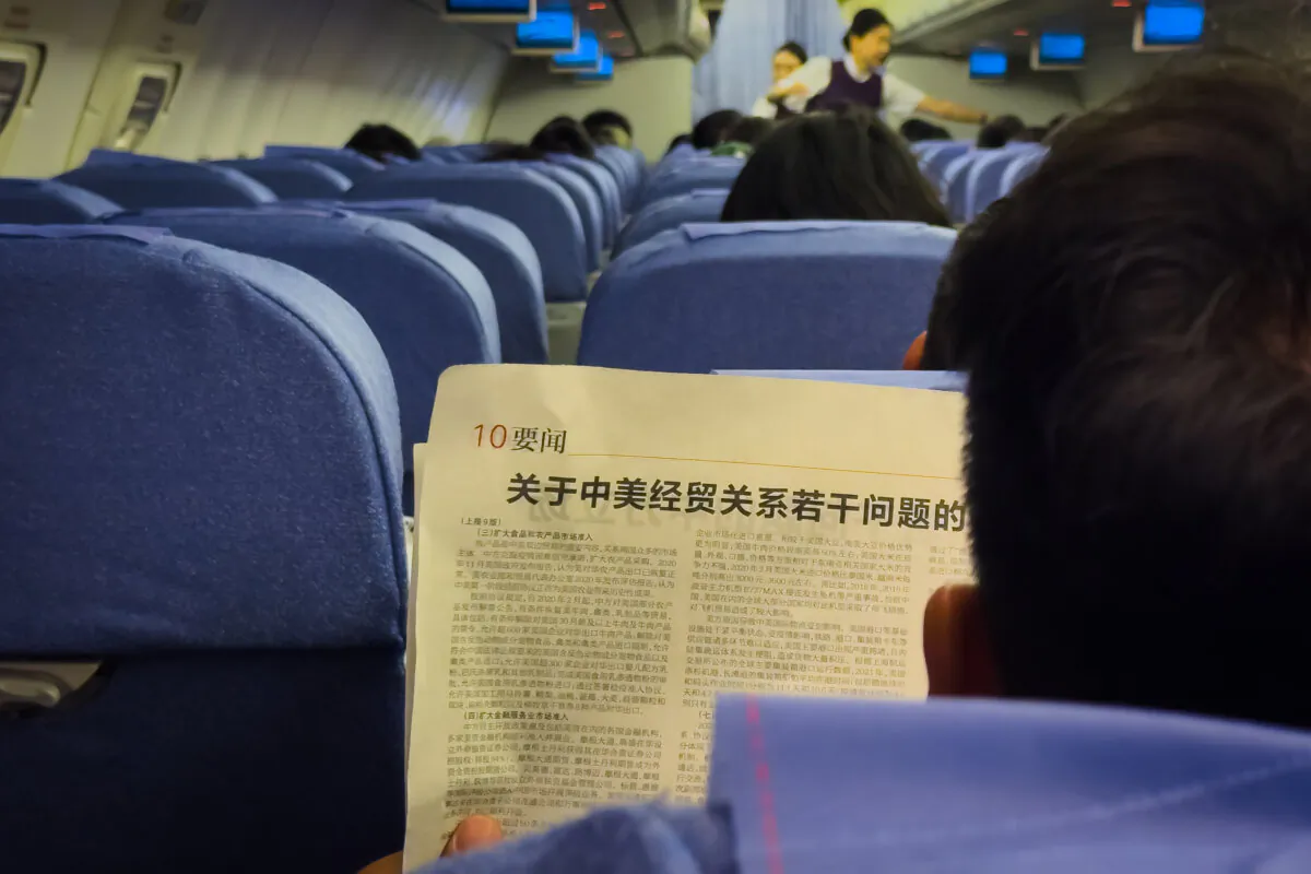An airline passenger, traveling from from Chongqing to Shenzhen, reads a newspaper article titled "China's Position on Several Issues Concerning China-U.S. Economic and Trade Relations," part of a white paper released by China's State Council Information Office on April 9, 2025. (Cheng Xin/Getty Images)