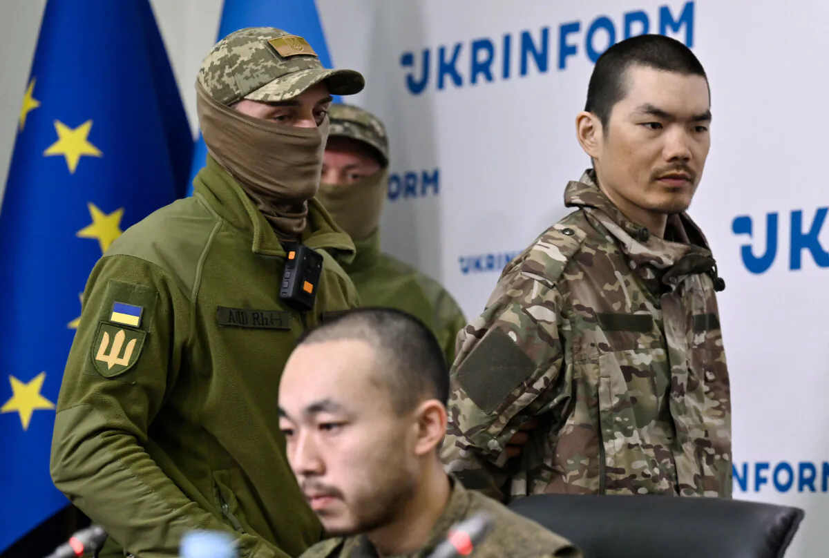 A serviceman of Security Service of Ukraine (SSU) escorts Chinese national Wang Guangjung (R) upon his arrival to attend a press conference with Chinese national Zhang Renbo (C) in Kyiv on April 14, 2025, amid the Russian invasion of Ukraine. Two Chinese nationals were captured by Ukrainian forces in the Donetsk region during what they claimed to be their first combat mission.  (Genya Savilov / AFP via Getty Images)