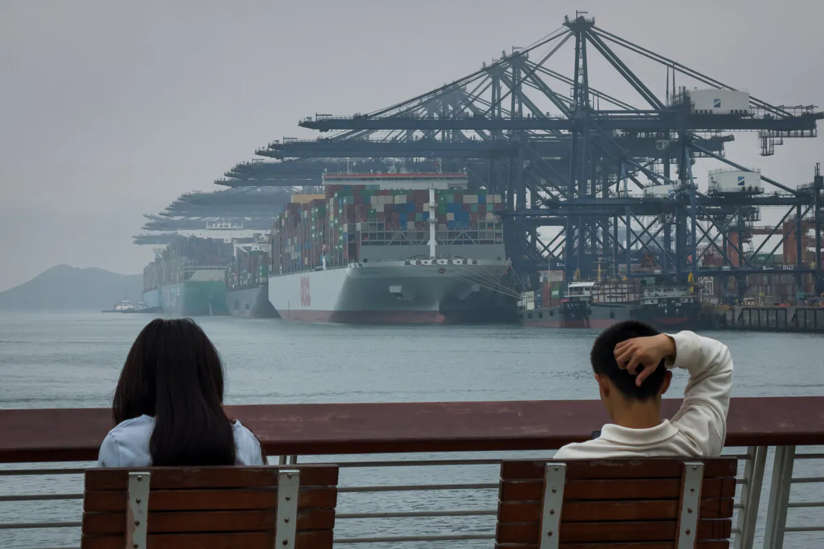 A man and a woman sit on a bench facing the Yantian International Container Terminals, where massive container ships are docked beneath rows of gantry cranes, in Shenzhen, China, on April 11, 2025. (Cheng Xin/Getty Images)