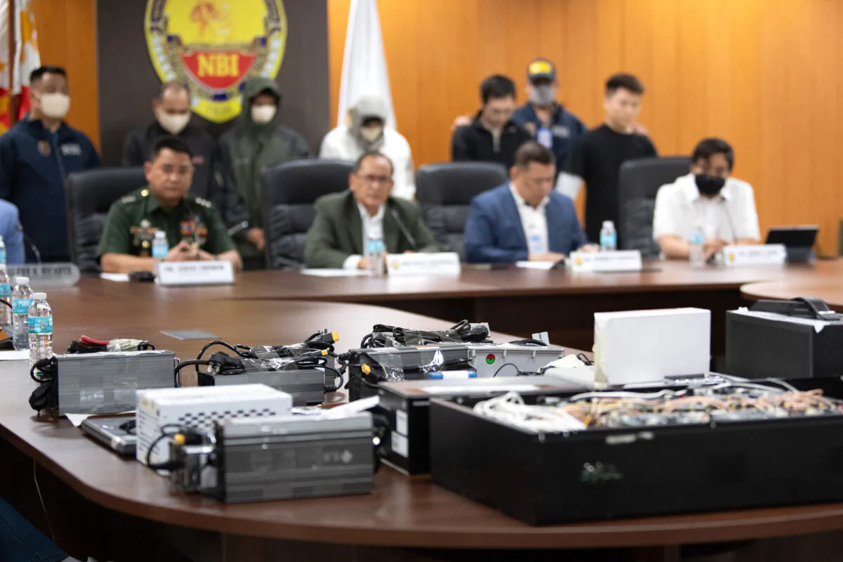 Seized equipment placed on display as Chinese nationals (background 3rd R and R) and their alleged Filipino accomplices (2nd L to 4th L) are presented behind (seated L-R) Armed Forces of the Philippines Public Affairs Office chief Colonel Xerxes Trinidad, National Bureau of Investigation (NBI) chief Jaime Santiago, NBI deputy chief for operations Antonio Pagatpat, and cybercrime unit chief Jeremy Lotoc during a press conference at the NBI office in Manila on Feb. 25, 2025. (Ted Aljibe/AFP via Getty Images)