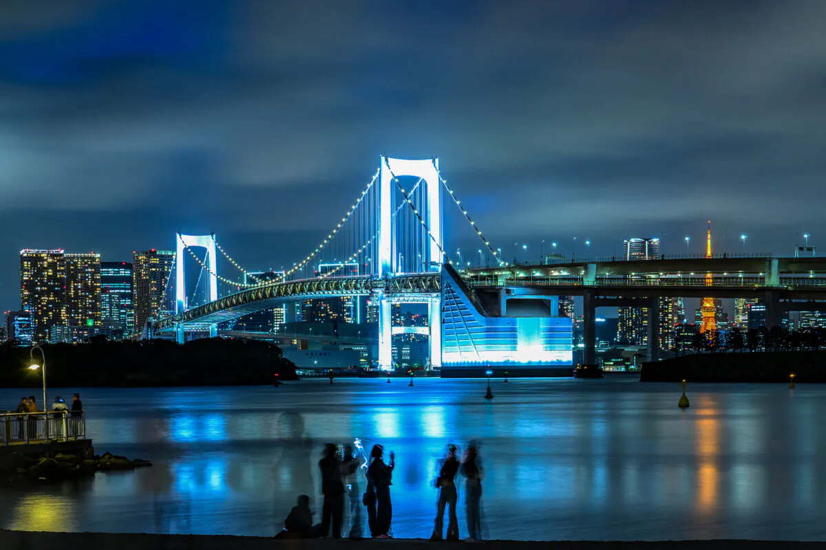 People stand along the beach as the Rainbow Bridge (back), which is part of the metropolitan expressway network, is seen from he Odaiba Marine Park in Tokyo on May 1, 2025. (Philip Fong/AFP via Getty Images)