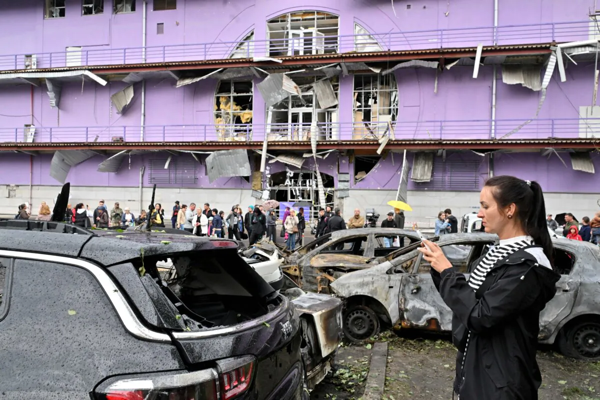 A woman takes pictures at burned vehicles outside a shopping mall following a night-time drone attack on Kyiv, on May 4, 2025 amid the Russian invasion of Ukraine. (Sergei Supinsky/AFP via Getty Images)