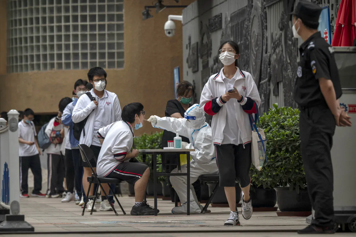 A student is given a nucleic acid test to detect COVID-19 by a health worker in protective clothing after finishing the final day of the National College Entrance Examination, also known as Gaokao, at a high school in Beijing on June 10, 2022. (Kevin Frayer/Getty Images)