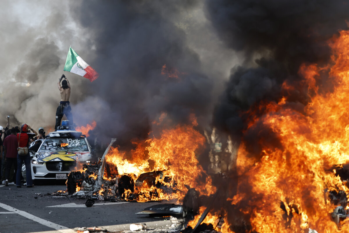 A protestor holds up a Mexican flag as burning cars line the street in Los Angeles, California, on June 08, 2025. (Mario Tama/Getty Images)