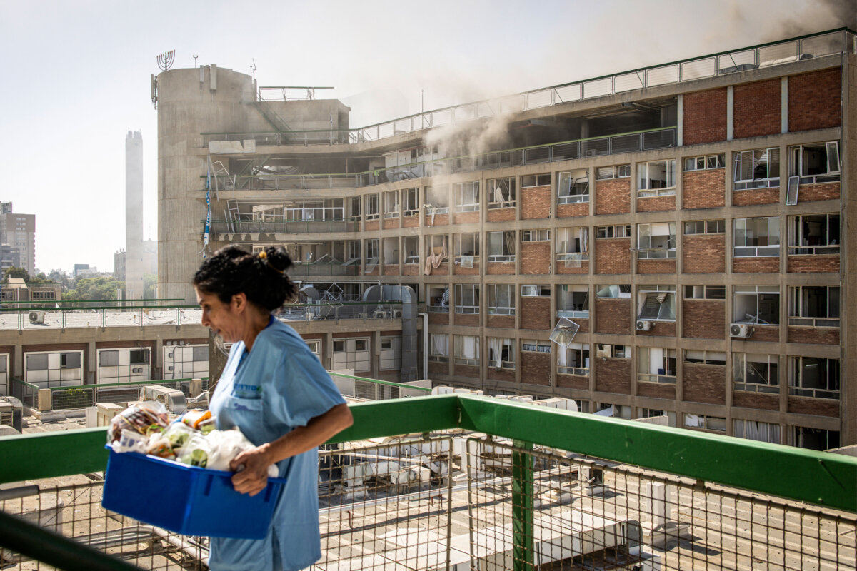 A nurse carries medical supplies past a building with smoke billowing out at Soroka Hospital following an Iranian missile attack in Beersheba in southern Israel on June 19, 2025. Soroka Hospital and two towns near Tel Aviv were struck in a barrage of Iranian missiles, with rescuers reporting at least 47 people injured. (John Wessels/AFP via Getty Images)