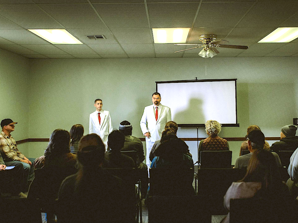 father and son wear white suits and give a talk to an audience in Sovereign.