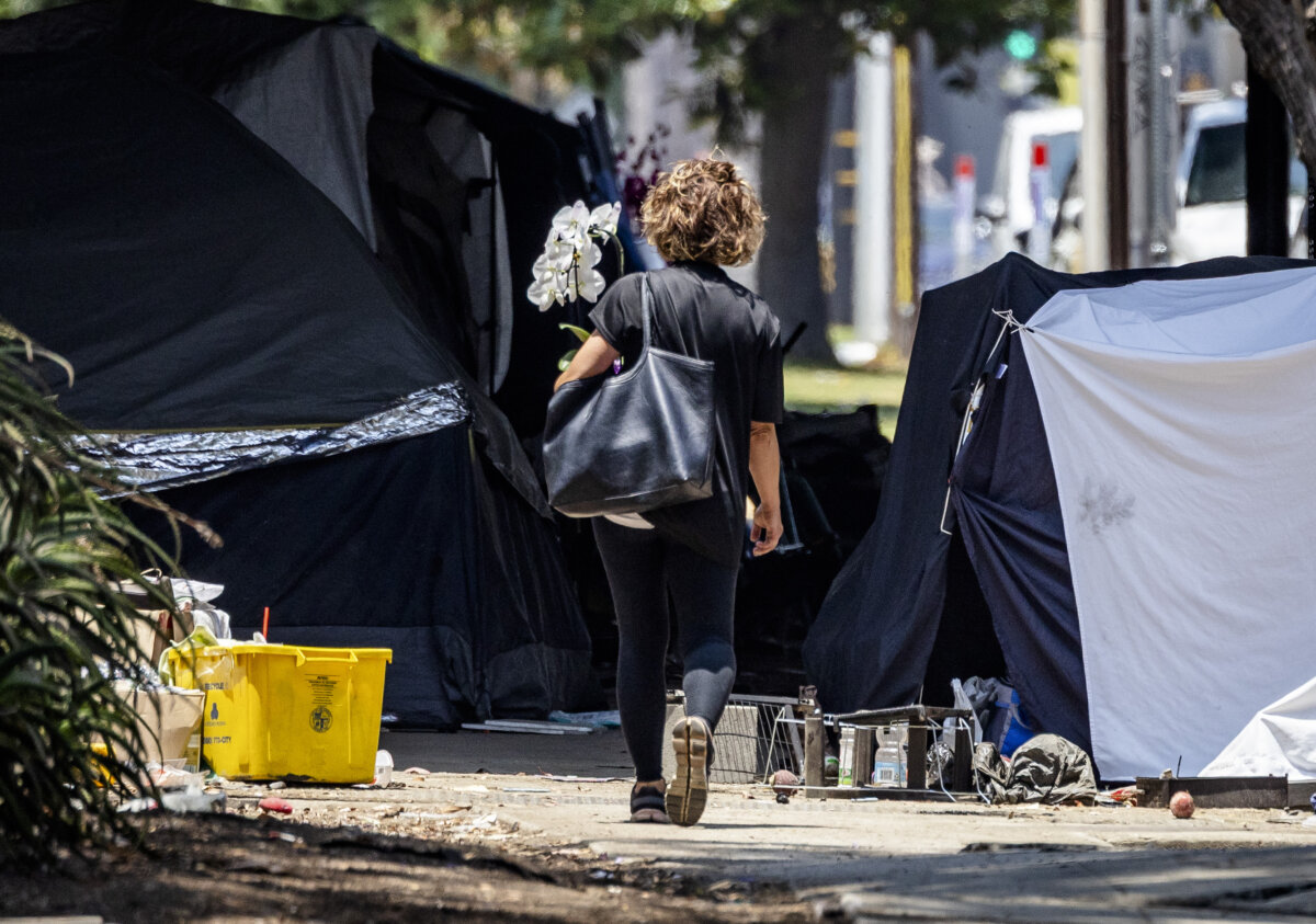 A woman prepares to pass a homeless encampment in Los Angeles on July 14, 2025. (John Fredricks/The Epoch Times)