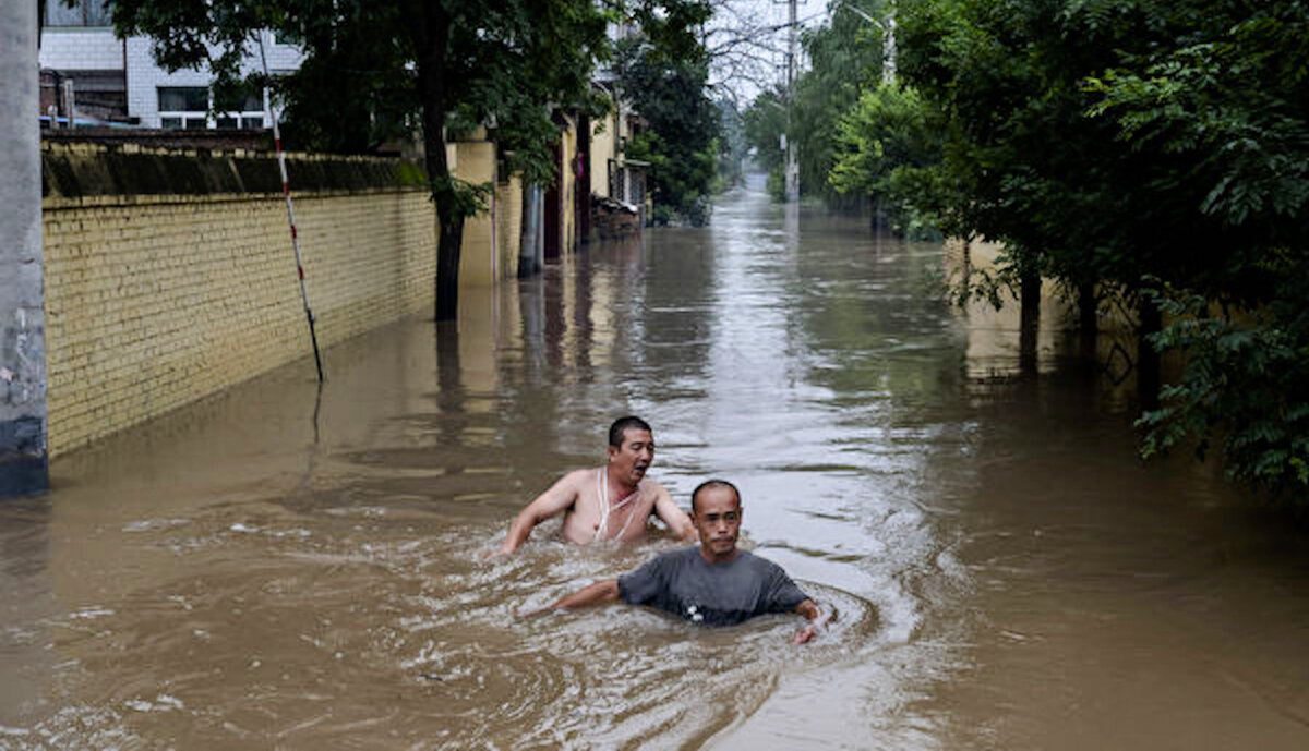 Local residents struggle in deep fast-moving water as they make their way toward rescuers in a boat in an area inundated with floodwaters near Zhuozhou, Hebei Province, south of Beijing, on Aug. 3, 2023. (Kevin Frayer/Getty Images)