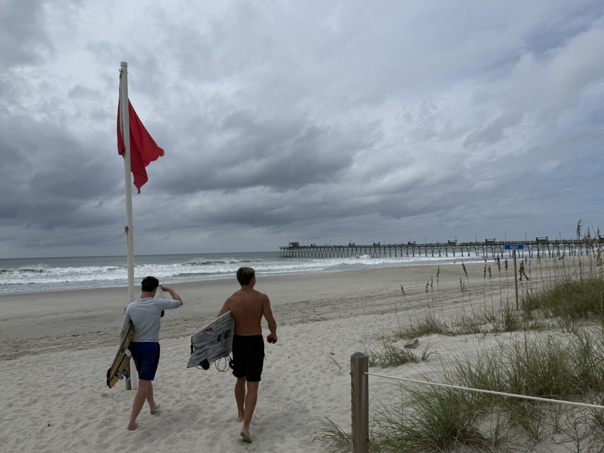 Jack Moore (L) and Owen Mohr prepare to surf near Bogue Inlet Fishing Pier on Emerald Isle, N.C., on Aug. 20, 2025. (T.J. Muscaro/The Epoch Times)