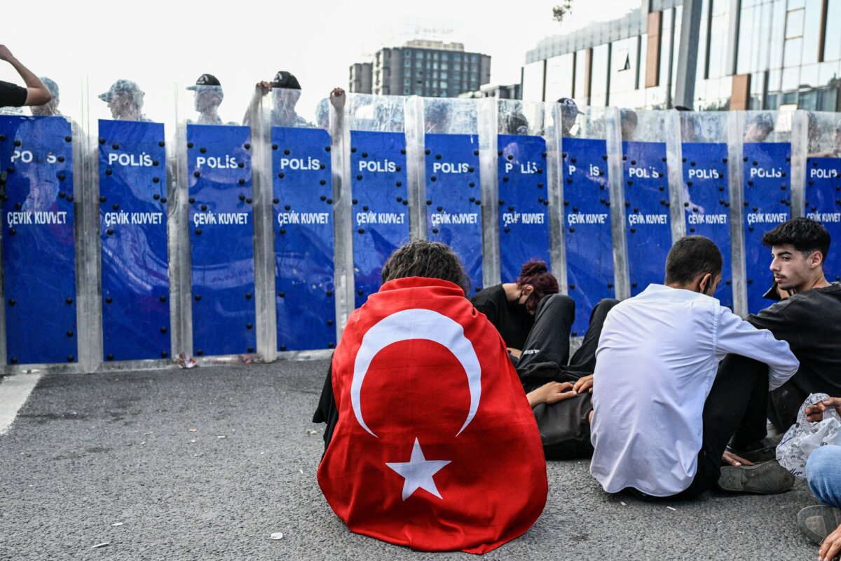 A protester wrapped in a Turkish flag sits in front of Turkish riot police as they block the entrance of the CHP's Istanbul headquarters on Sept. 8, 2025. (Kemal Aslan/AFP via Getty Images)