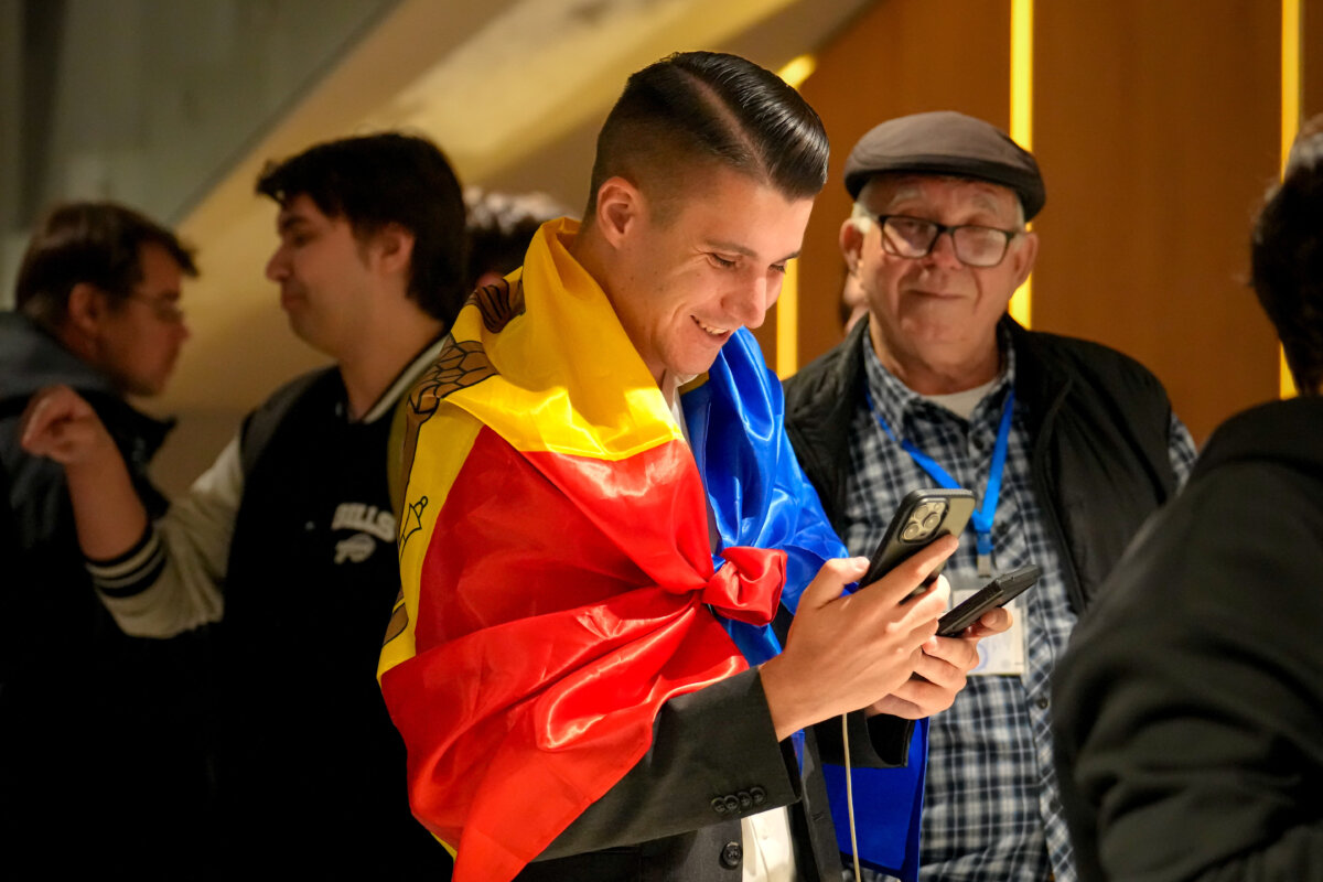 A supporter of the pro-EU Party of Action and Solidarity draped in the Moldovan flag smiles as he checks partial results on a phone after the polls closed for the parliamentary election in Chisinau, Moldova, on Sept. 28, 2025. (Vadim Ghirda/AP)