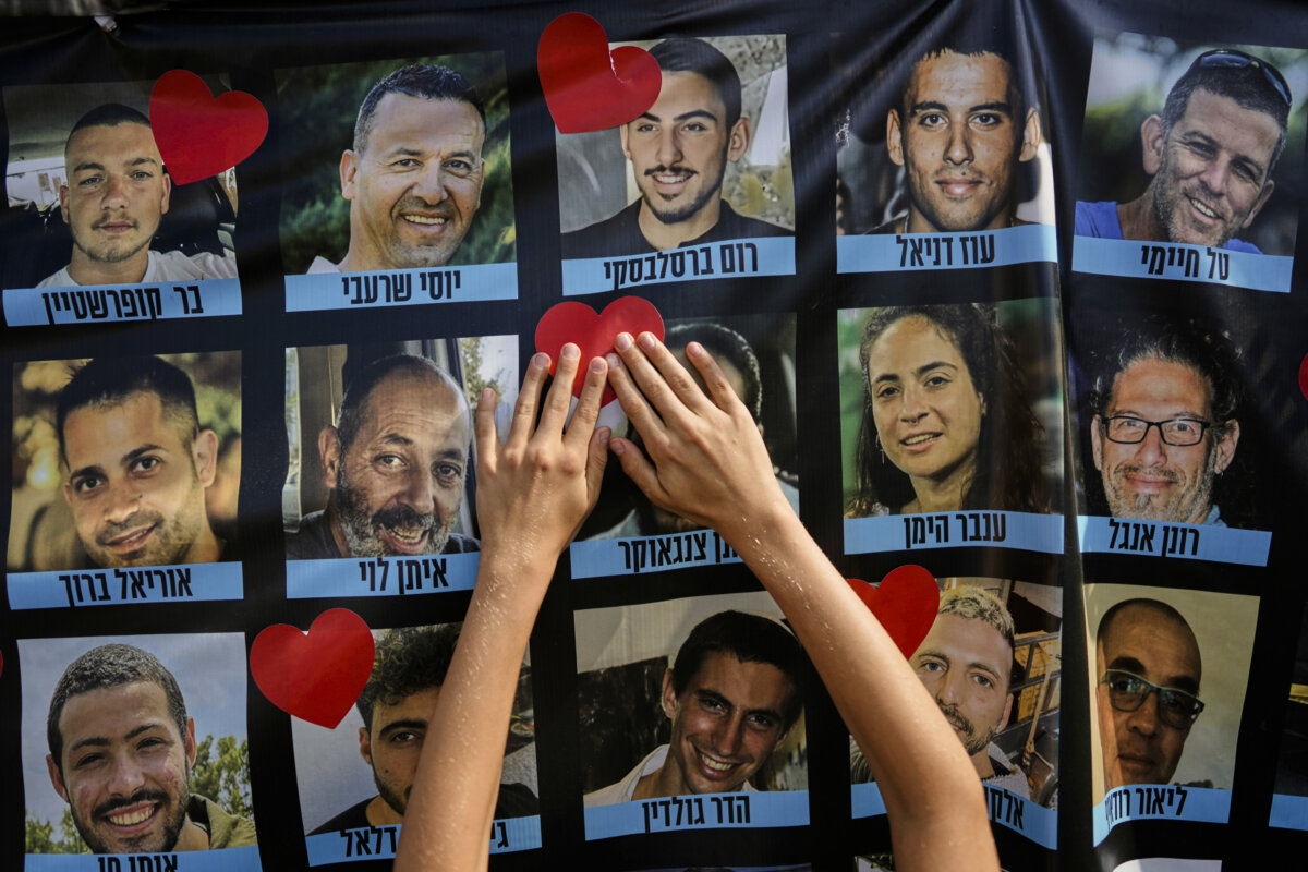 A person pastes a heart-shaped sticker on a banner with pictures of Israeli hostages during a a gathering at a plaza known as hostages square in Tel Aviv, Israel, Monday, Oct. 13, 2025. (AP Photo/Oded Balilty)