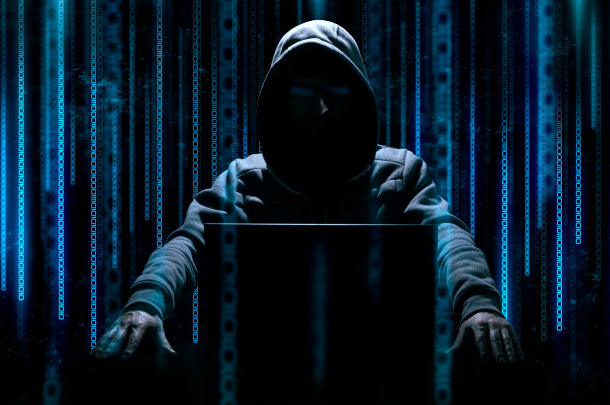 Hacker sits behind laptop with binary code on background