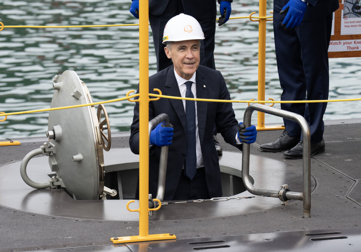 Prime Minister Mark Carney smiles as he climbs down a ladder into a submarine during a tour of the Hanwha Ocean Shipyard in Geoje Island, South Korea, on Oct. 30, 2025. (The Canadian Press/Adrian Wyld)