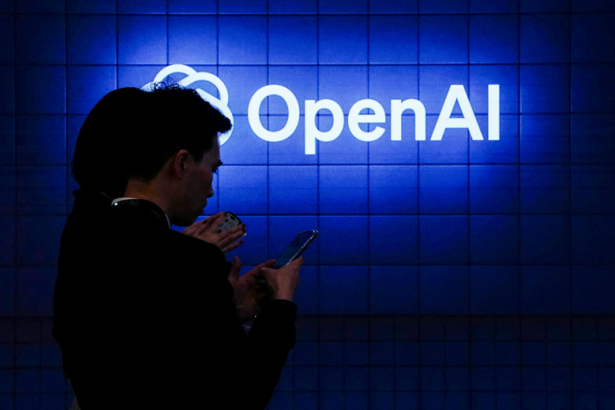 A visitor looks at their phone next to an Open AI logo during the Mobile World Congress in Barcelona on Feb. 26, 2024. (Pau Barrena/AFP via Getty Images)