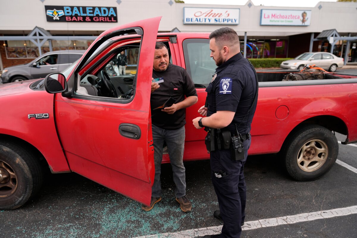 Willy Aceituno (L) makes a police report with Charlotte-Mecklenburg Police Department officer N. Sherill, claiming that his window was broken during a U.S. Customs and Border Protection enforcement operation in Charlotte, N.C., on Nov. 15, 2025. (Erik Verduzco/AP Photo)