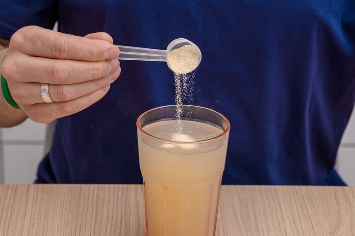 A man dissolving a scoop of collagen in a glass of water, dietary supplements.