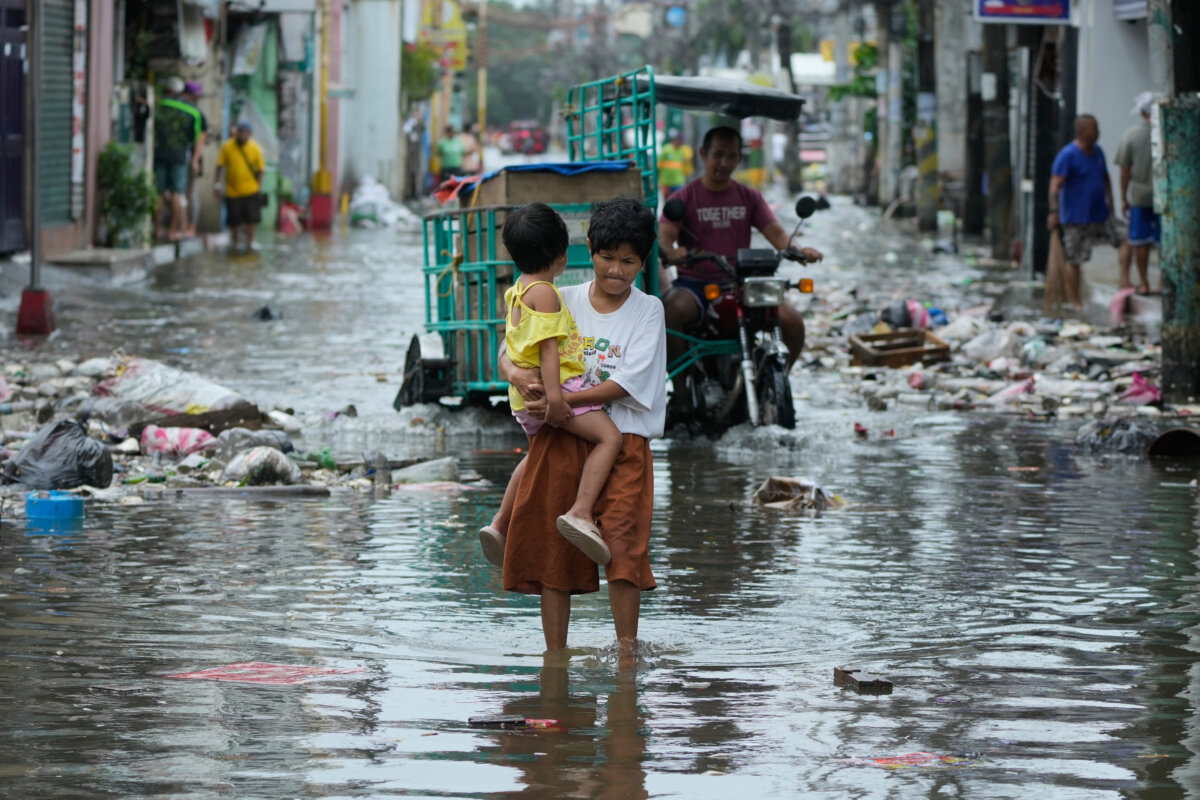 A woman and child crosses a flooded street due to Typhoon Fung-wong and high tide on Monday, Nov. 10, 2025, in Navotas, Philippines. (Aaron Favila/AP Photo)