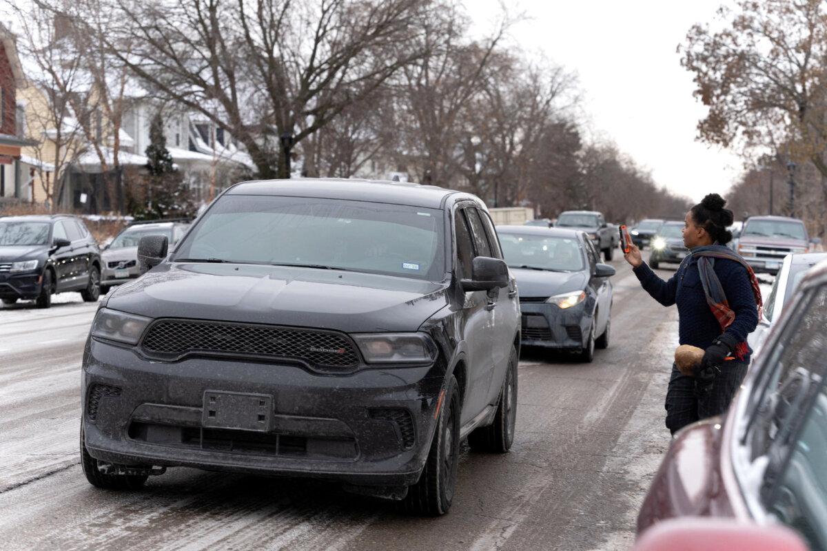 A rapid response community observer holds their phone as a vehicle carrying federal agents drives by during an immigration raid on a home in the South Minneapolis area on Dec. 4, 2025. (Tim Evans/Reuters)