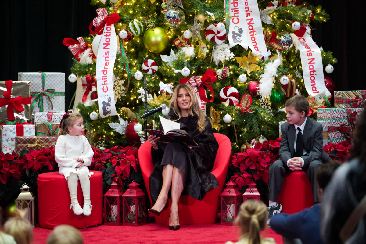 First Lady Melania Trump, accompanied by two children, patients Faith Hinkle (L) and Riley Whitney (R), reads "How Does Santa Go Down the Chimney?" by Mac Barnett, illustrated by Jon Klassen, during a visit to Children’s National Hospital in Washington on Dec. 5, 2025. (Madalina Kilroy/The Epoch Times)
