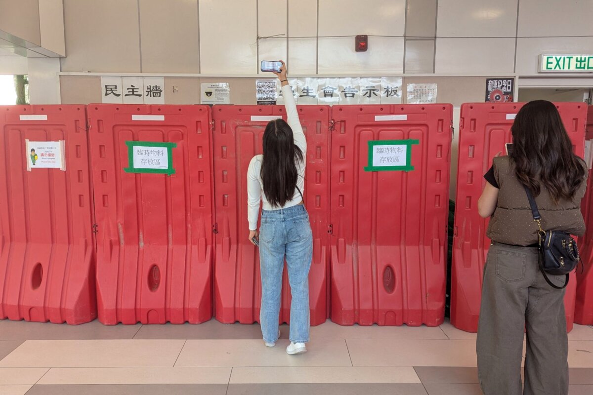A woman takes a photo with her phone above barricades in front of the student union-run notice board, nicknamed "democracy wall", at Hong Kong Baptist University in Hong Kong on Dec. 3, 2025. (Holmes Chan/AFP via Getty Images)