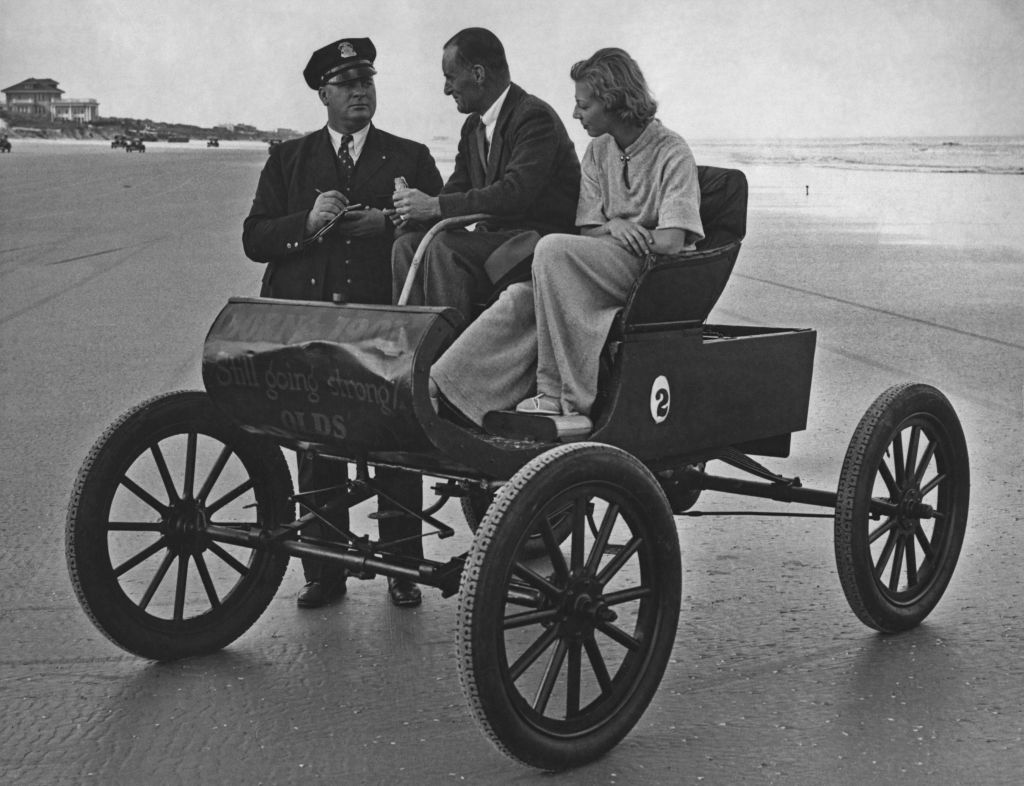 A police officer writes a ticket for a couple sitting in an Oldsmobile Curved Dash runabout on a beach, circa 1935. Painted on the front of the car are the words "Born in 1905, still going strong. Olds." (Keystone View Company/FPG/Archive Photos/Getty Images)