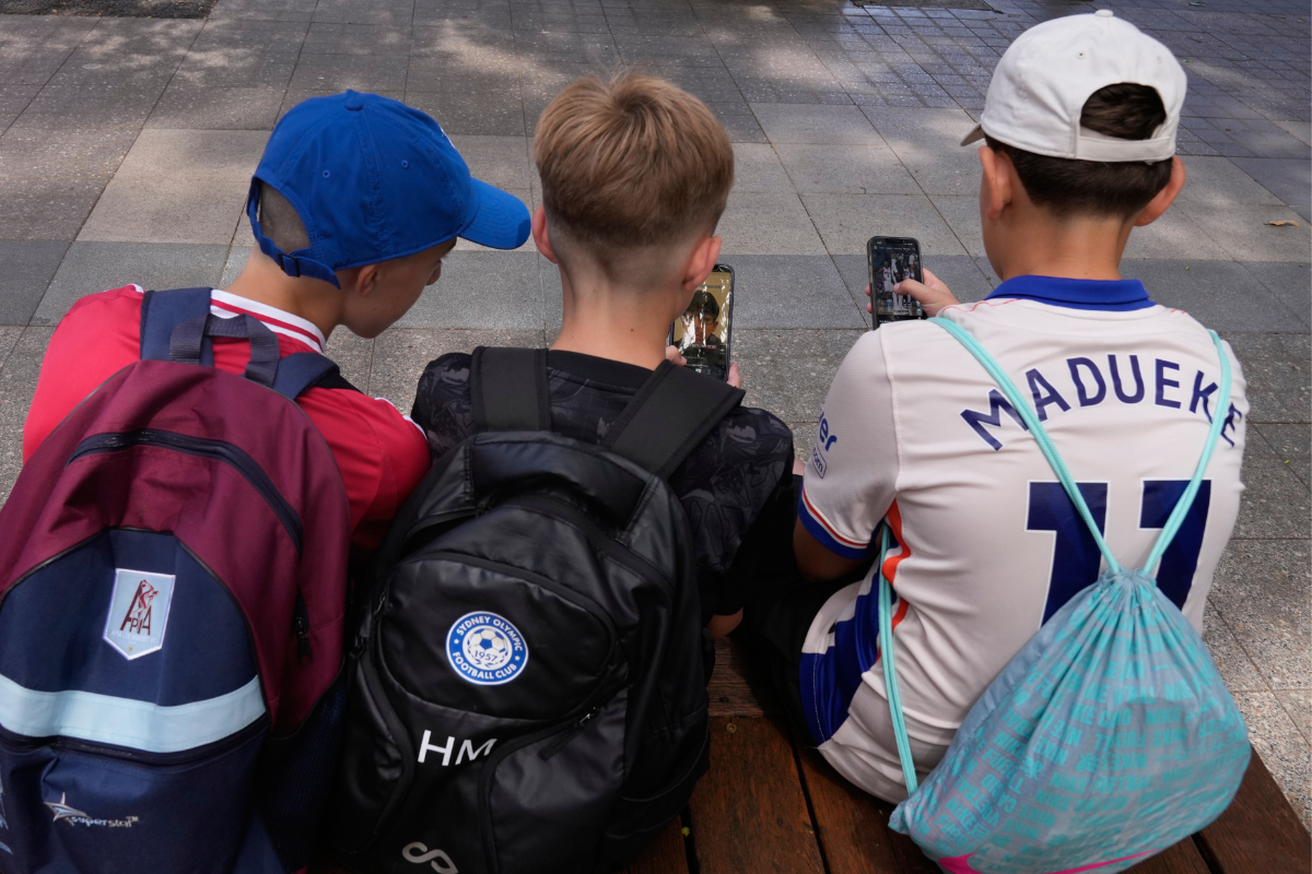 Three 11-year-old boys use their phones while sitting outside a school in Sydney on Dec. 8, 2025. (Rick RycroftAP Photo)
